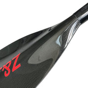 Close-up of a glossy carbon fiber paddle blade showing the weave pattern of the ZJ Full Carbon Fiber Flatwater Canoe Paddle (Unassembled) by ZJ SPORT. A red design, possibly a logo or lettering, is on the left side, ideal for flatwater adventures.