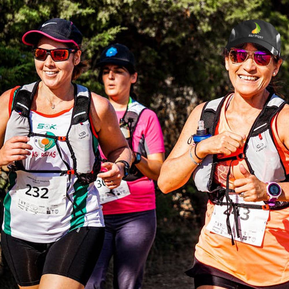 Three women participate in an outdoor run wearing Z&J SPORT Unisex Quick Dry Adjustable Unstructured Caps by ZJ SPORT, smiling as they jog on a tree-lined path. Two runners wear white and orange tops, enjoying UV protection from their caps.