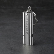 Engraved with ZJ SPORT, the ZJ Stainless Steel Emergency Survival Whistle rests on a dark surface, featuring a double tube design for emergencies and includes a keyring clip along with a carabiner and lanyard for easy attachment.