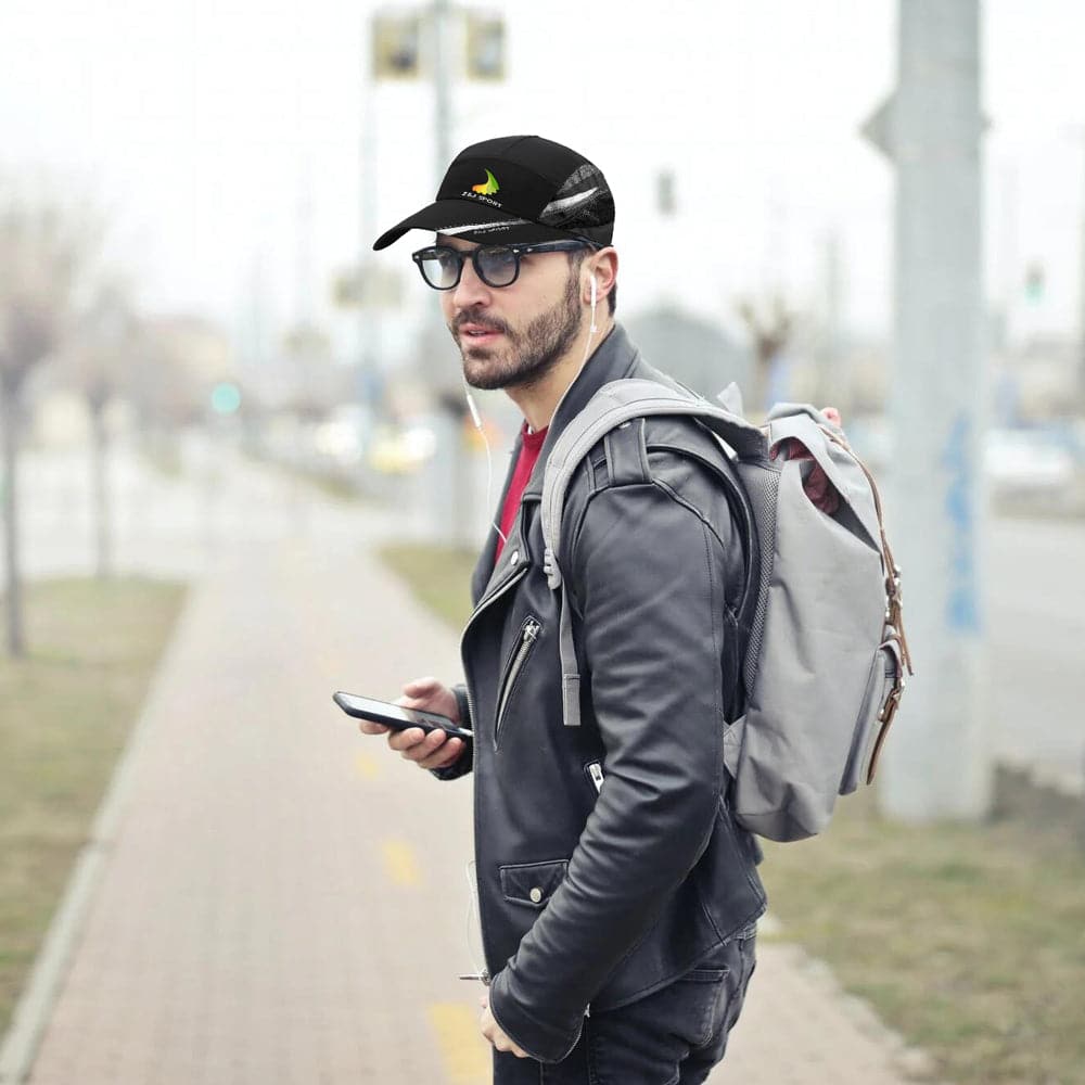A man in sunglasses, a Z&J SPORT Unisex Quick Dry Adjustable Cap, and a leather jacket holds a smartphone on the sidewalk. He wears earbuds and has a gray backpack against a blurry cityscape background.
