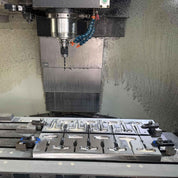 A zijie 5 Axis CNC milling machine from the Mold Design (OEM Service) lineup is in operation, precisely cutting a pattern into a securely clamped metal sheet, with the spindle hovering and metal shavings scattered around.