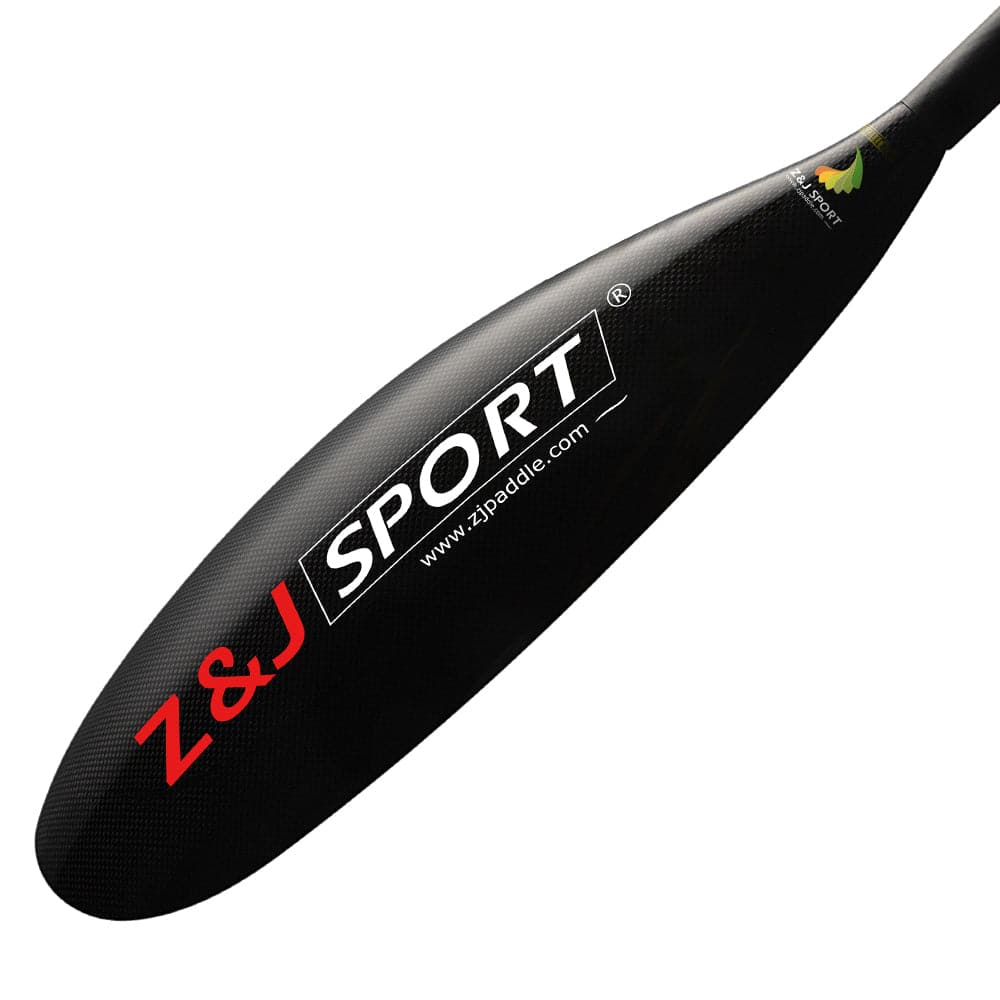 Close-up of a ZJ SPORT carbon fiber kayak paddle blade with Z&J SPORT and www.zjpaddle.com in bold white and red text. The paddle, from the ZJ X Series, has a textured surface, reinforced edge, asymmetrical shape, and features a small colorful logo near the tip.