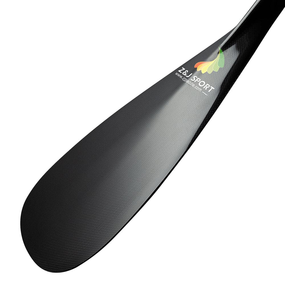 A close-up of the ZJ Hybrid Outrigger Canoe Paddle features a sleek carbon fiber-textured black blade, adorned with the colorful ZJ SPORT logo and website. The blade transitions smoothly into the handcrafted wood shaft with an anti-skid grip.