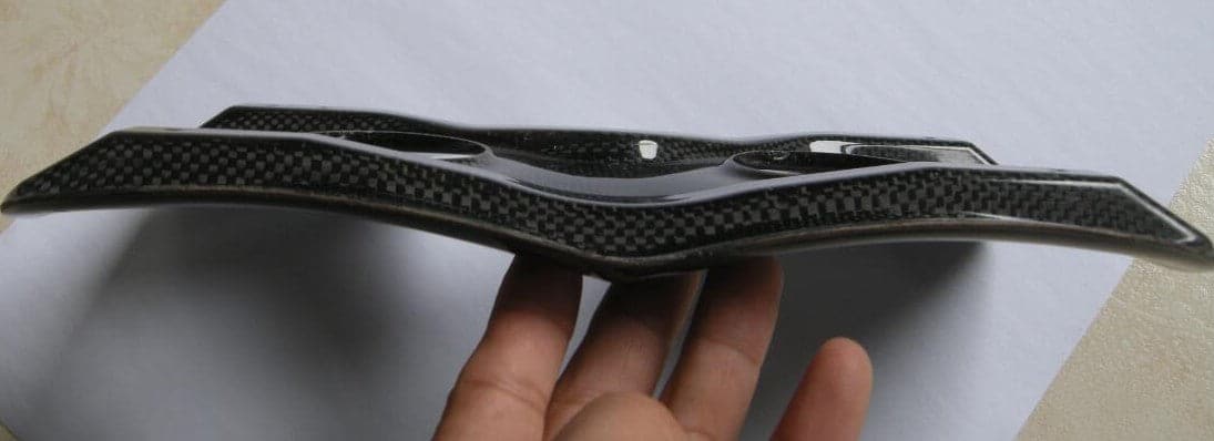 A person holds a ZJ SPORT ZJ High Quality Carbon Fiber Seat Top Pad for Racing Rowing Boats against a white background. The pad, with its sleek boat-inspired design, features a glossy finish that accentuates the woven carbon fiber pattern. [Free Shipping].